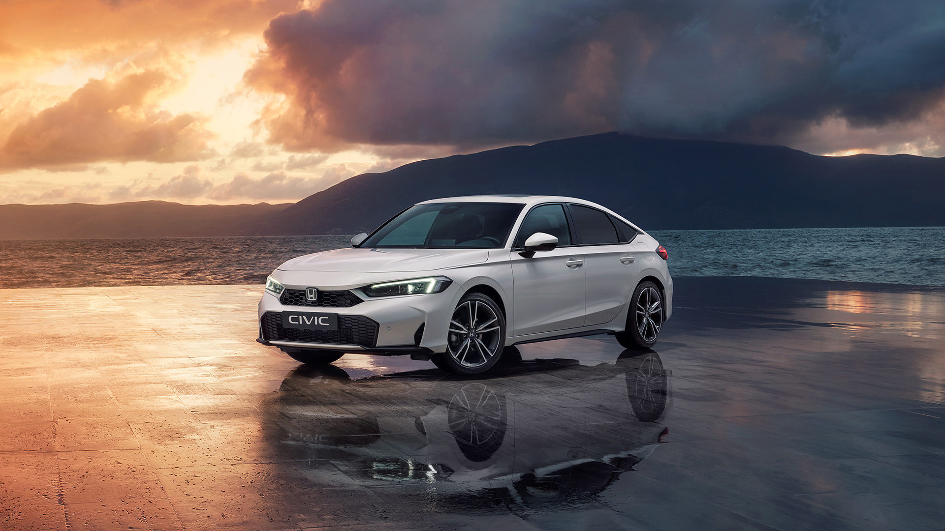 Civic Hybrid zaparkovaný pri oceáne pri západe slnka.