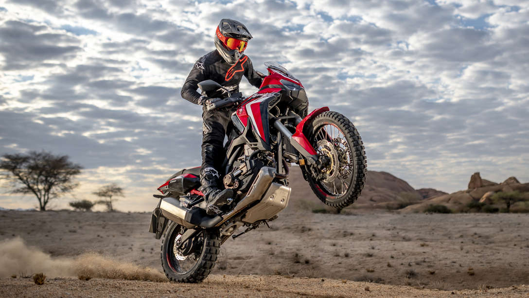 Trojštvrťový pohľad spredu z pravej strany na model Honda Africa Twin pri jazde so zdvihnutým predným kolesom v púšti