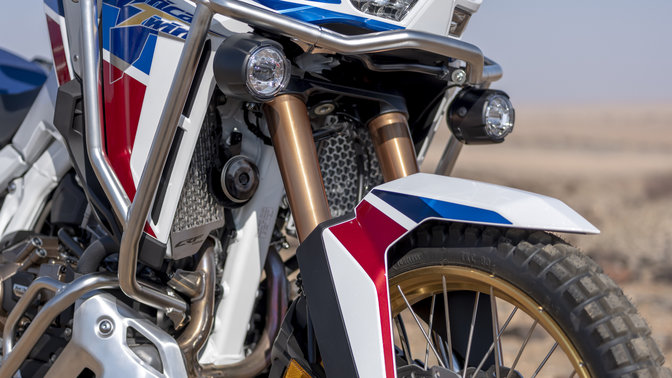 Záber spredu na model Honda Africa Twin Adventure Sports so zapnutými svetlami v púšti