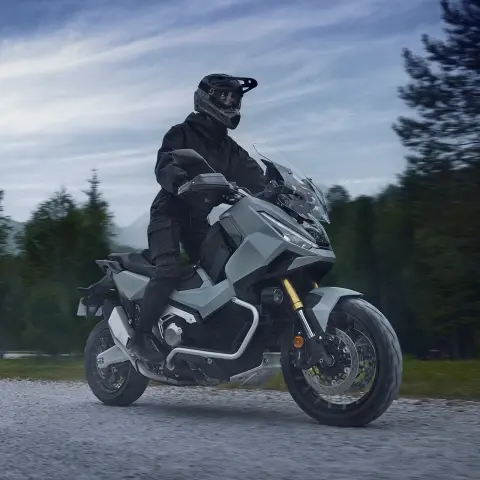 Trojštvrťový záber spredu na skúter X-ADV na štrku so stojacim jazdcom
