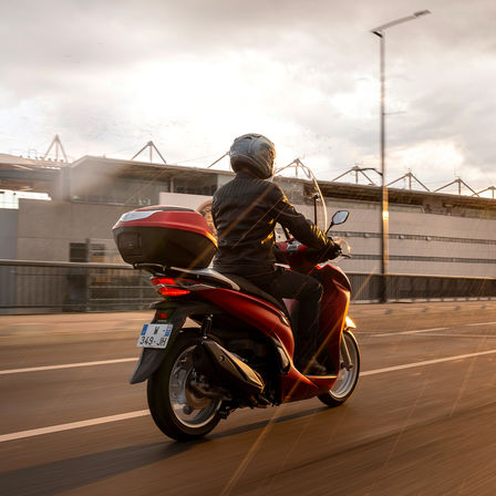 Honda SH350i, trojštvrťový zadný záber z pravej strany, s jazdcom, červený motocykel