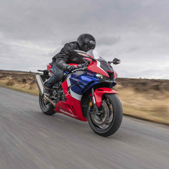 Honda CBR1000RR-R Fireblade, trojštvrťový záber spredu z pravej strany, s jazdcom na vidieckej ceste, červený motocykel